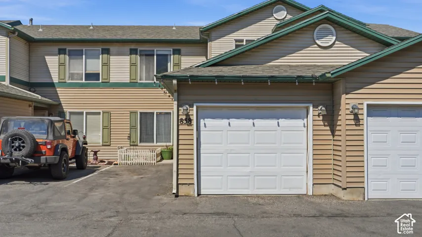 Multi-level exterior featuring tan siding with green trim, multiple windows with green shutters, and a front entry with a small patio area