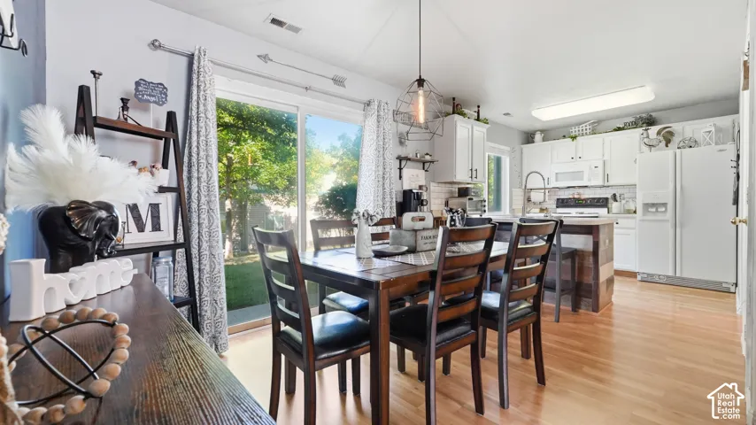 Open-concept dining area featuring wood-finish flooring, a contemporary pendant light fixture, and a sliding glass door providing direct access to the backyard