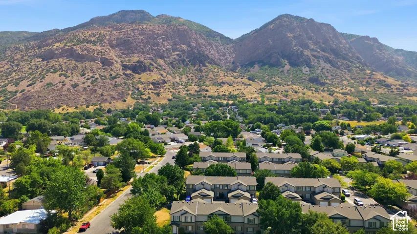 Expansive residential neighborhood set against a backdrop of prominent mountains, featuring numerous trees and varied housing architecture