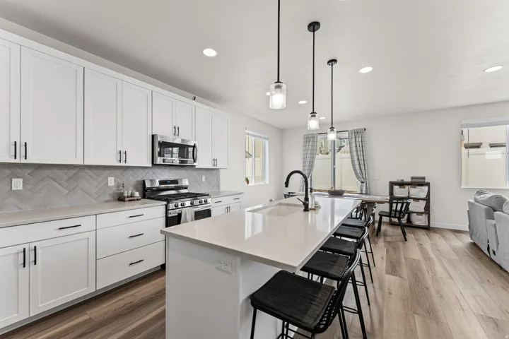 Modern kitchen featuring white cabinetry, a herringbone tile backsplash, stainless steel appliances, a large center island with seating, and recessed lighting