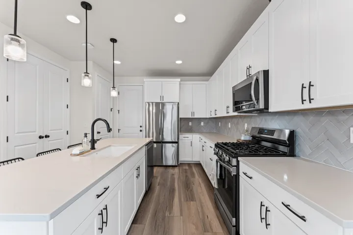 Kitchen featuring wood-finish flooring, white cabinetry with matte black hardware, stainless steel appliances, light-toned countertops, and a herringbone tile backsplash