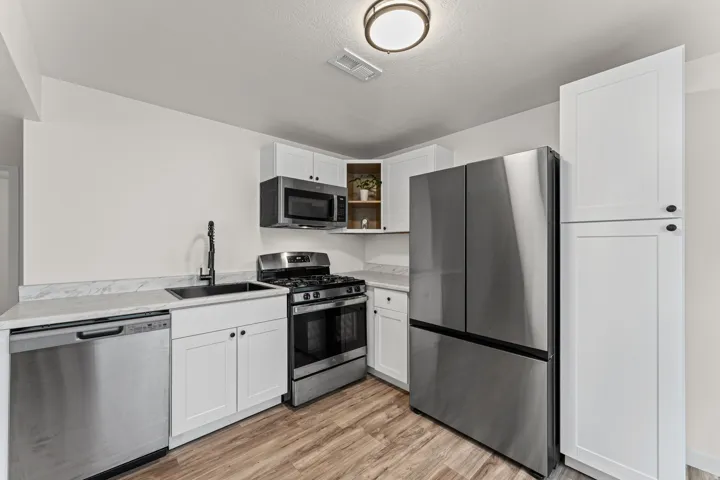 Kitchen featuring white cabinetry, stainless steel appliances, wood-finish flooring, a matte black faucet, and light-toned countertops