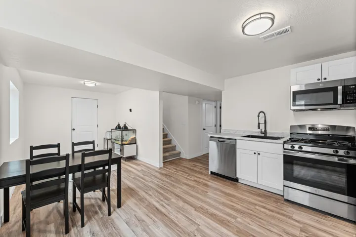 Open-concept living space featuring wood-finish flooring, a full kitchen with white cabinetry and stainless steel appliances, and ceiling-mounted lighting fixtures