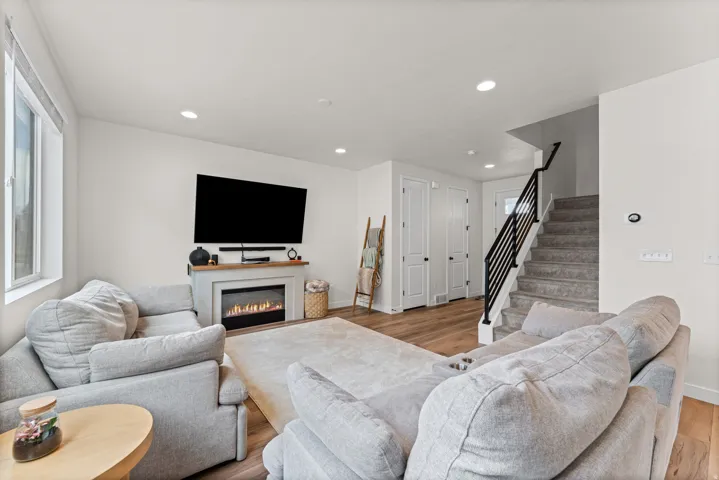 Living area featuring a modern fireplace with a light-toned mantel, wood-finish flooring, recessed lighting, and a staircase with a black metal railing