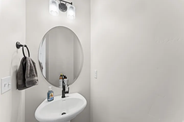Pedestal sink with a matte black faucet, oval mirror, and a two-light vanity fixture