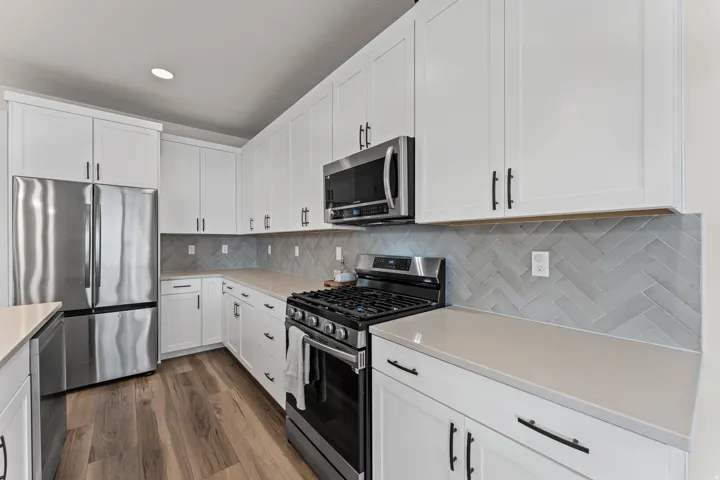 Modern kitchen featuring white cabinetry, stainless steel appliances, light-toned countertops, and wood-finish flooring