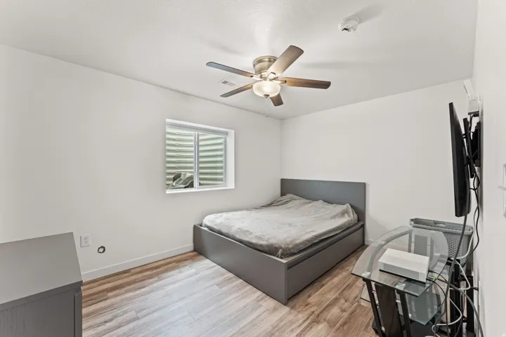 Room featuring wood-finish flooring, a ceiling fan with integrated lighting, and a window with horizontal blinds