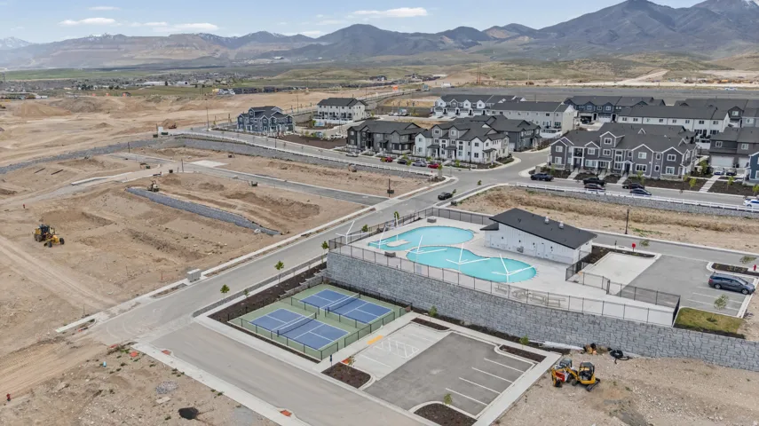 Community amenities featuring a swimming pool, two pickleball courts, and a parking area, surrounded by modern residential structures and undeveloped land