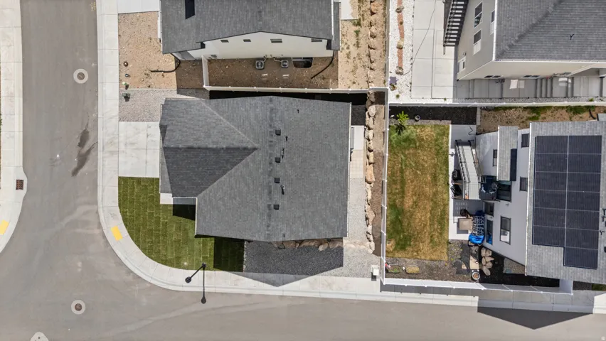 Newly constructed home featuring a dark shingle roof, established corner lot with green lawn, concrete sidewalks, and surrounding gravel landscaping
