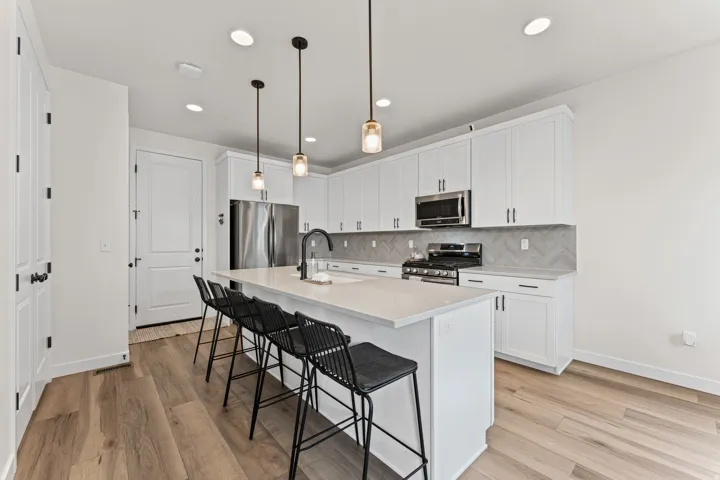 Modern kitchen featuring an expansive island with seating, white shaker cabinetry, stainless steel appliances, and a herringbone tile backsplash