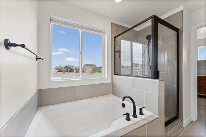 Bathroom featuring a built-in soaking tub with matte black fixtures, a walk-in shower with a black-framed glass enclosure, and neutral-toned wall tiling