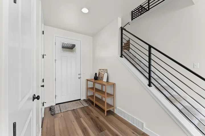 Entryway featuring wood-finish flooring, a white paneled front door with upper lite, and a contemporary staircase with black horizontal railings