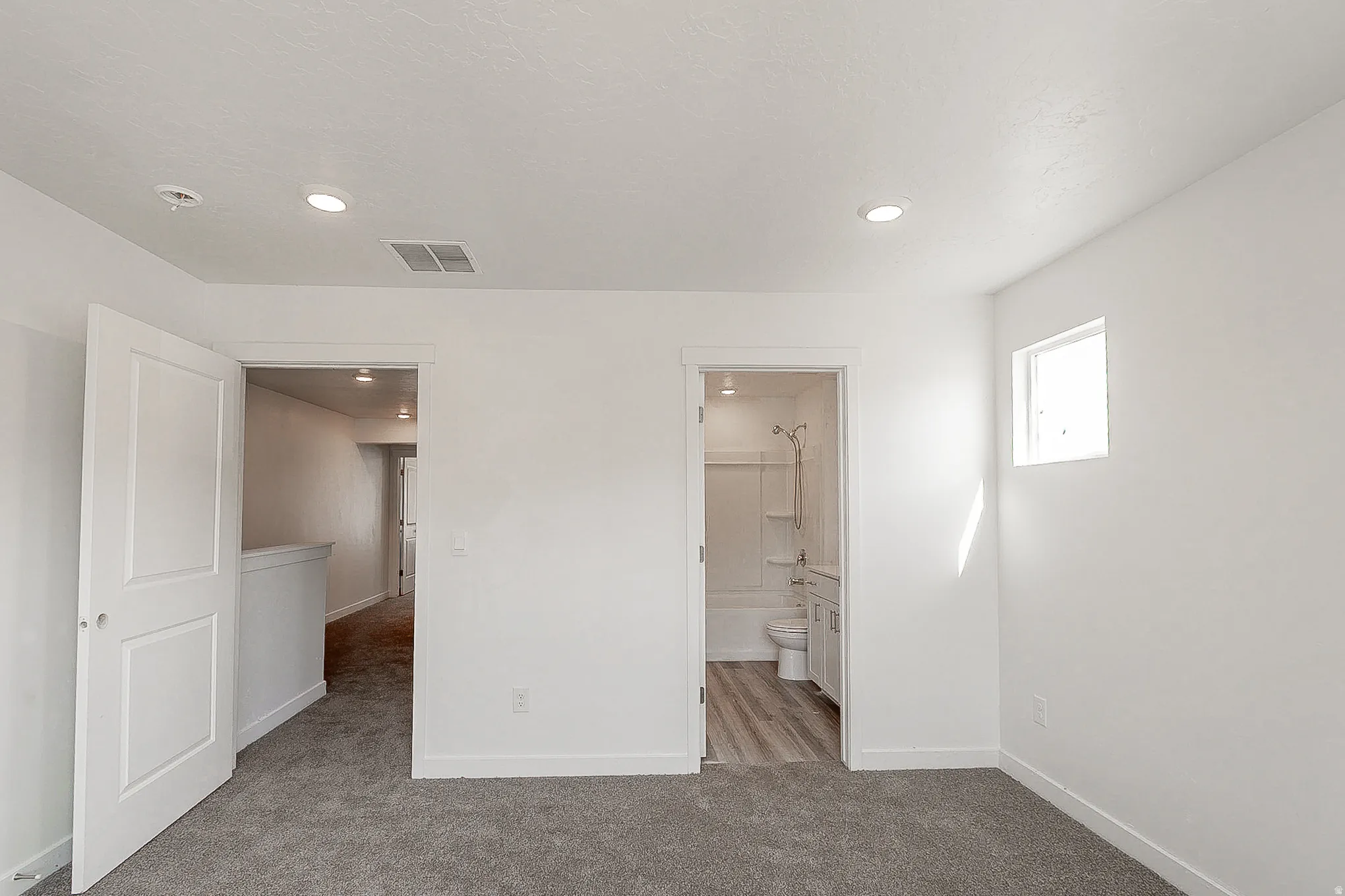 Bright primary bedroom with recessed ceiling lighting, multiple entry points, and direct access to an ensuite bathroom featuring tile shower surround