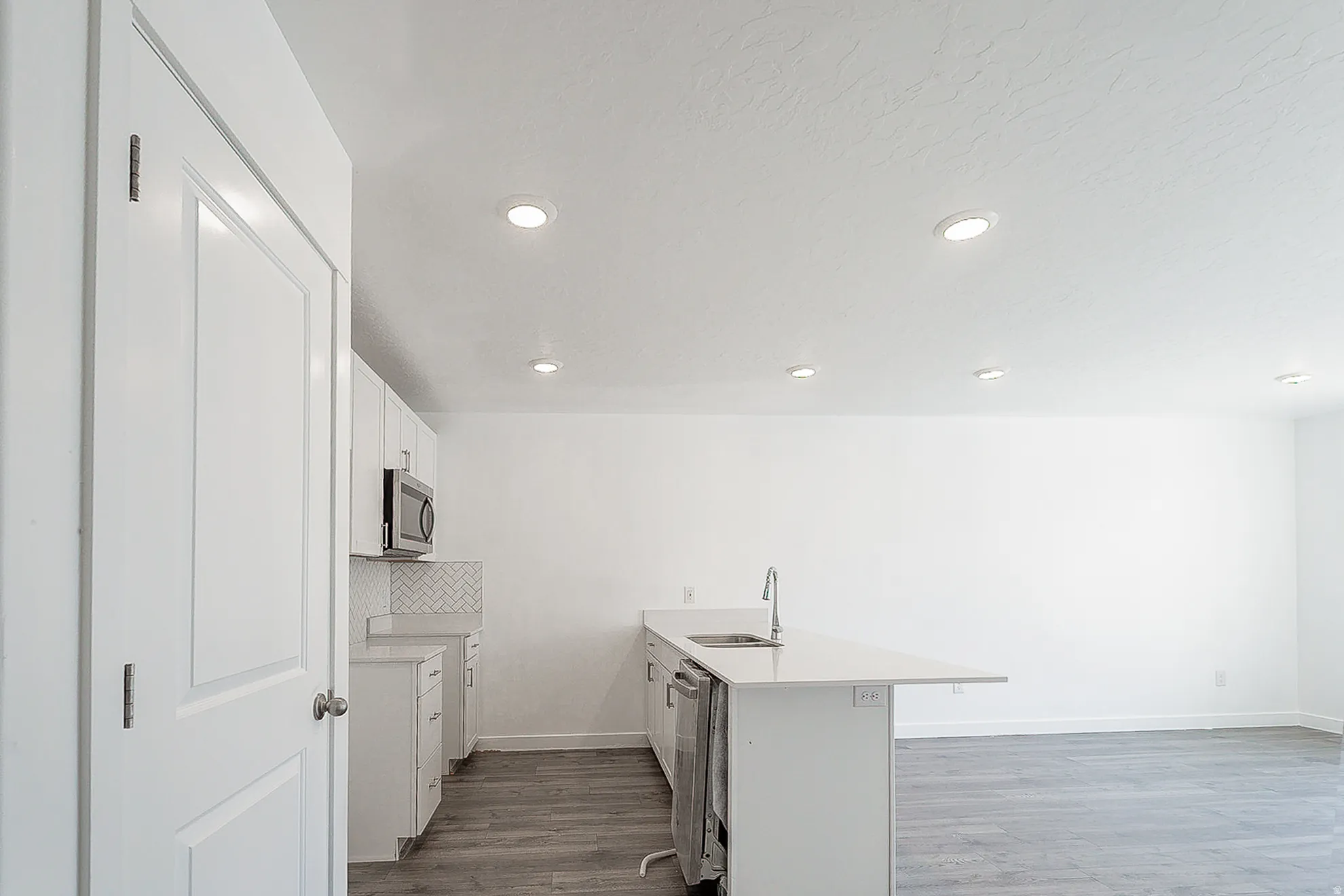 Contemporary kitchen featuring white cabinetry, stainless steel microwave, herringbone tile backsplash, and an island with an undermount sink