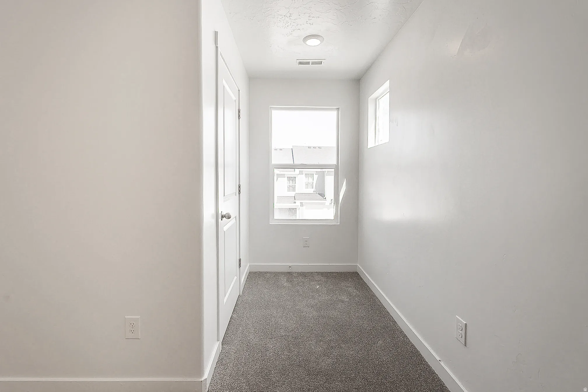 Bright hallway with recessed ceiling lighting, neutral white walls, and gray carpet flooring