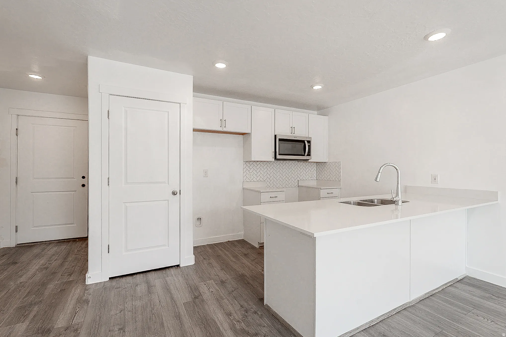 Modern kitchen featuring a spacious island with white cabinetry, stainless steel appliances including a microwave, quartz countertops, and a polished nickel faucet