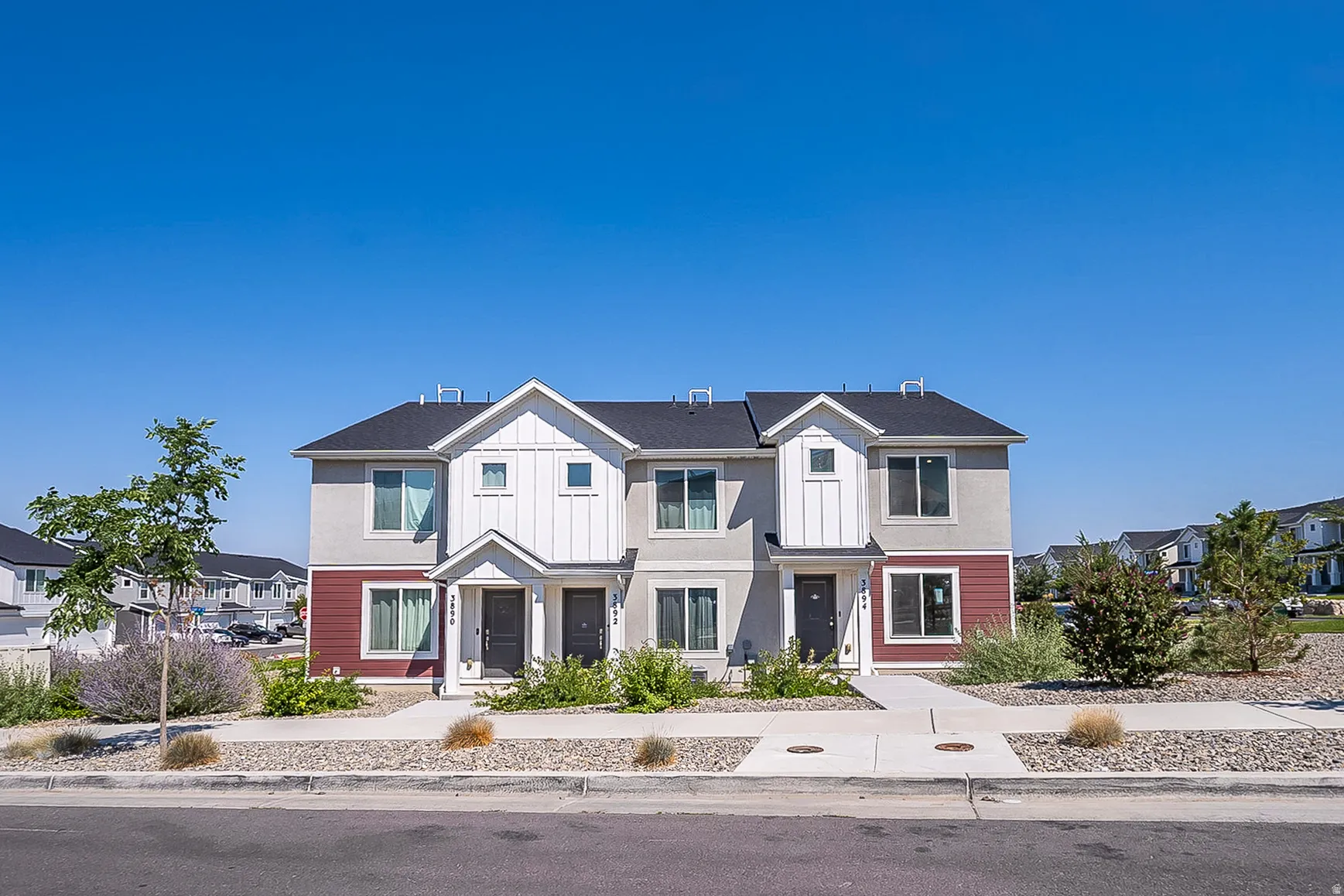 Modern multi-unit residential property featuring a striking two-tone exterior with white and burgundy fiber cement siding, peaked rooflines with architectural gables, and dark asphalt shingle roofing