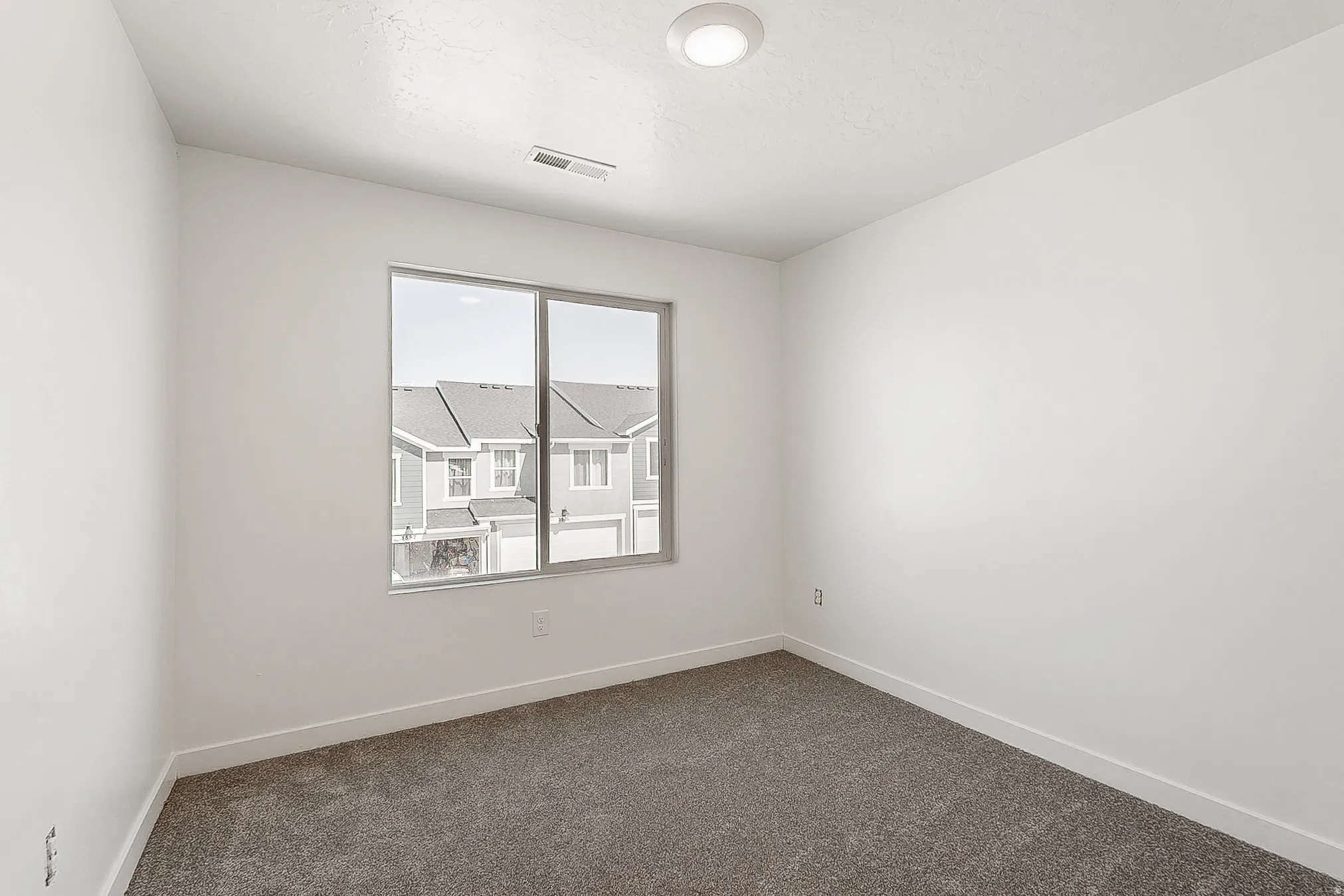 Room featuring a window with a neighborhood backdrop, white walls, gray carpet, and a recessed ceiling light