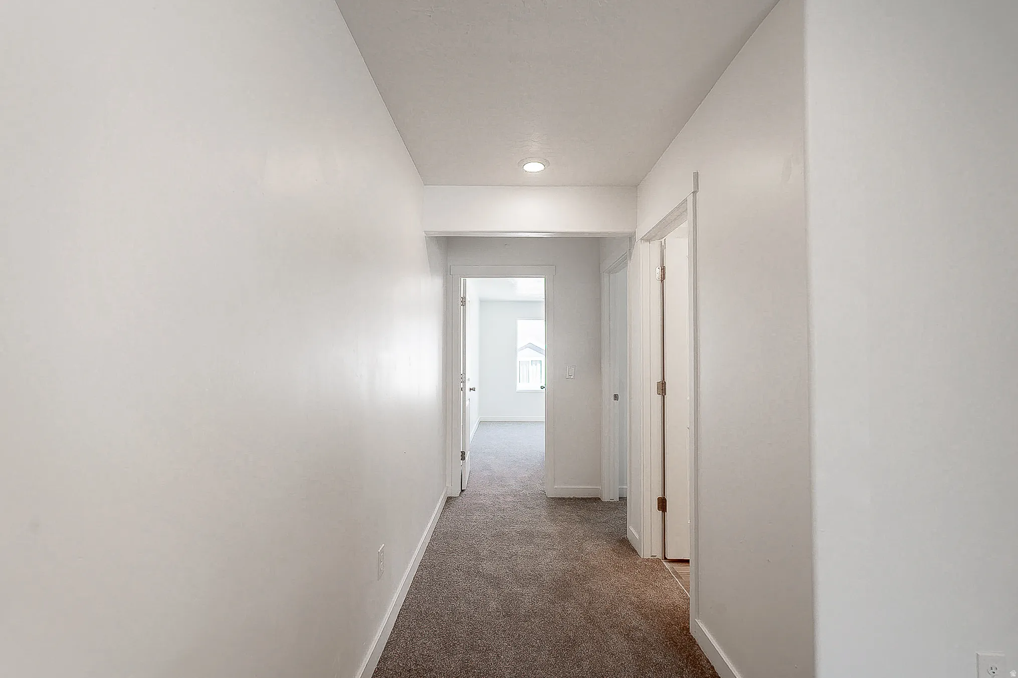 Bright hallway with recessed lighting and neutral wall finishes, featuring multiple white six-panel doors and warm wood-finish flooring throughout