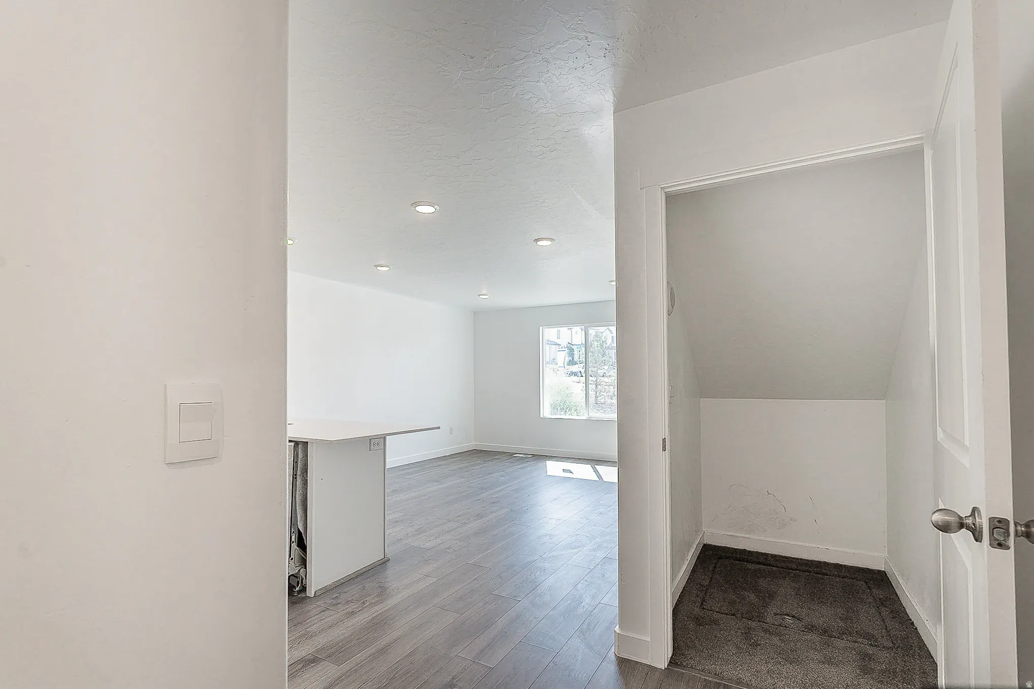 Modern open-concept living space featuring wood-finish flooring, recessed ceiling lighting, and clean white walls with minimal trim detailing