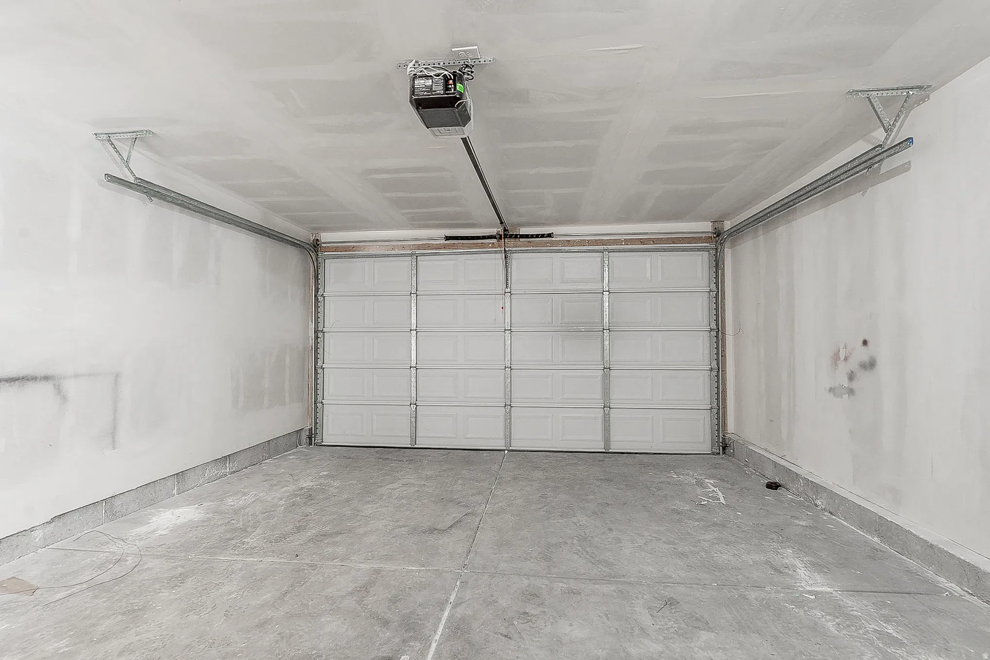 Spacious garage with a sectional overhead door, exposed ceiling joists, concrete flooring, and an automatic garage door opener mechanism