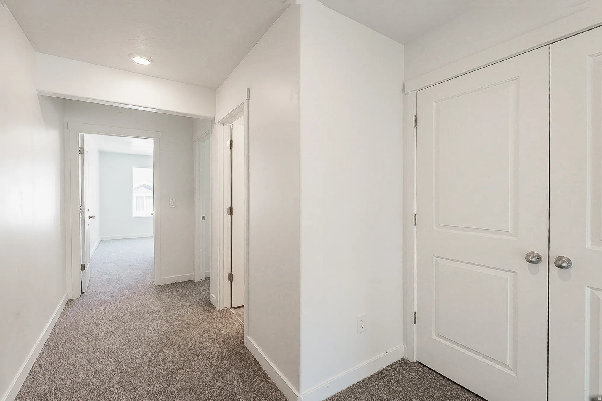 Spacious hallway with neutral carpet flooring, recessed ceiling lighting, and abundant natural light from the entry