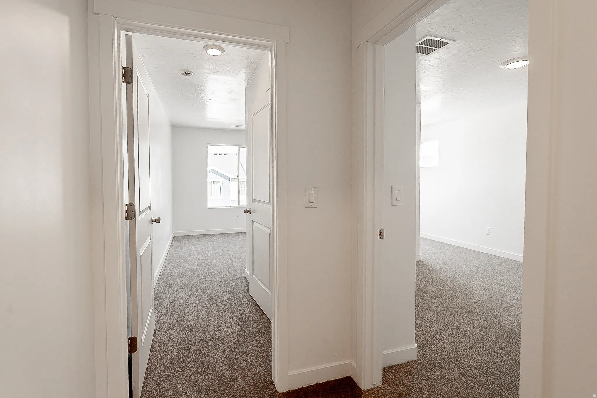 Bright hallway featuring clean white walls, recessed ceiling lighting, and neutral carpet flooring throughout