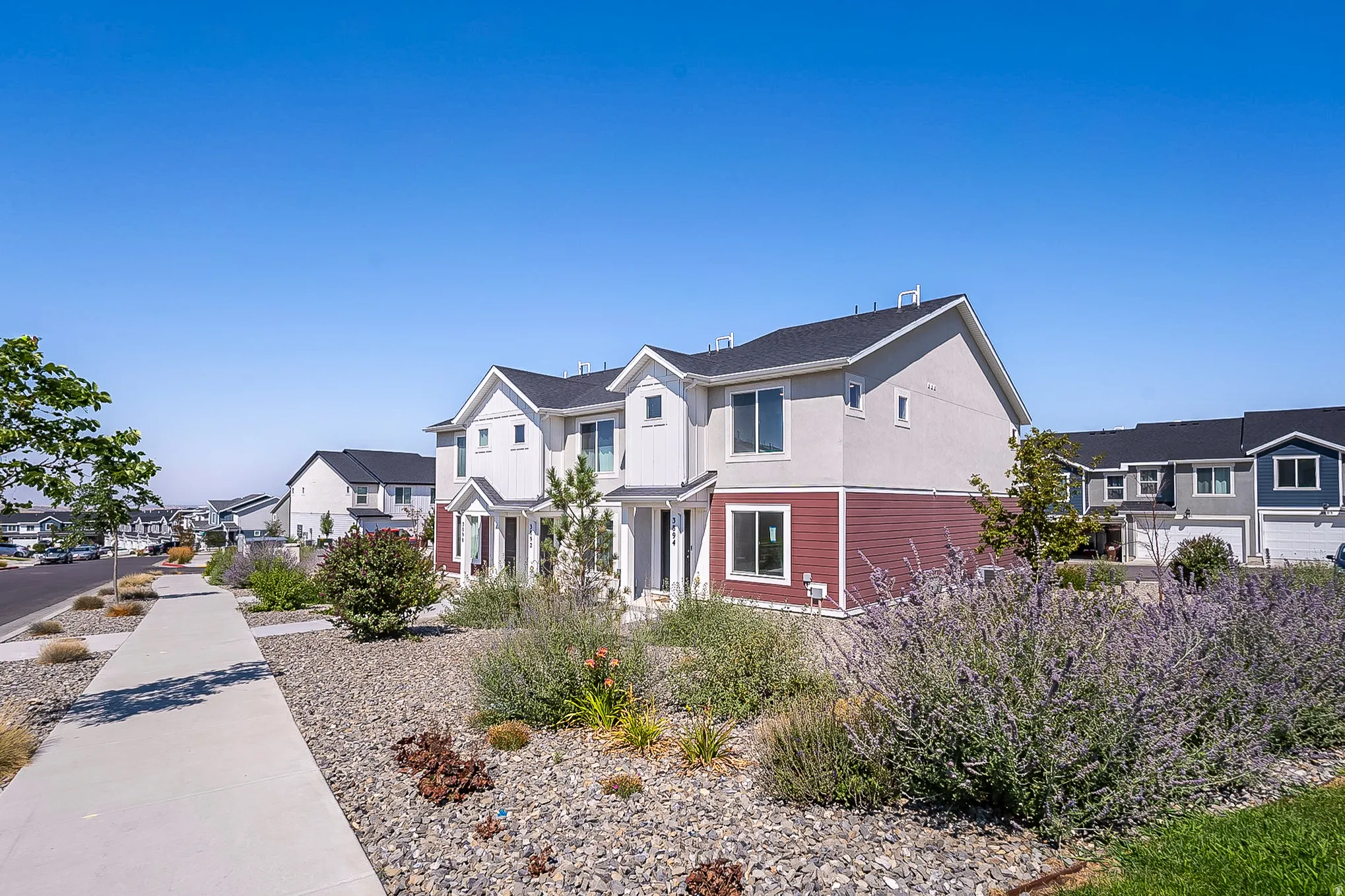 Contemporary townhome exterior featuring clean architectural lines, mixed material facade, dark shingle roofing, and established landscaping with a concrete sidewalk