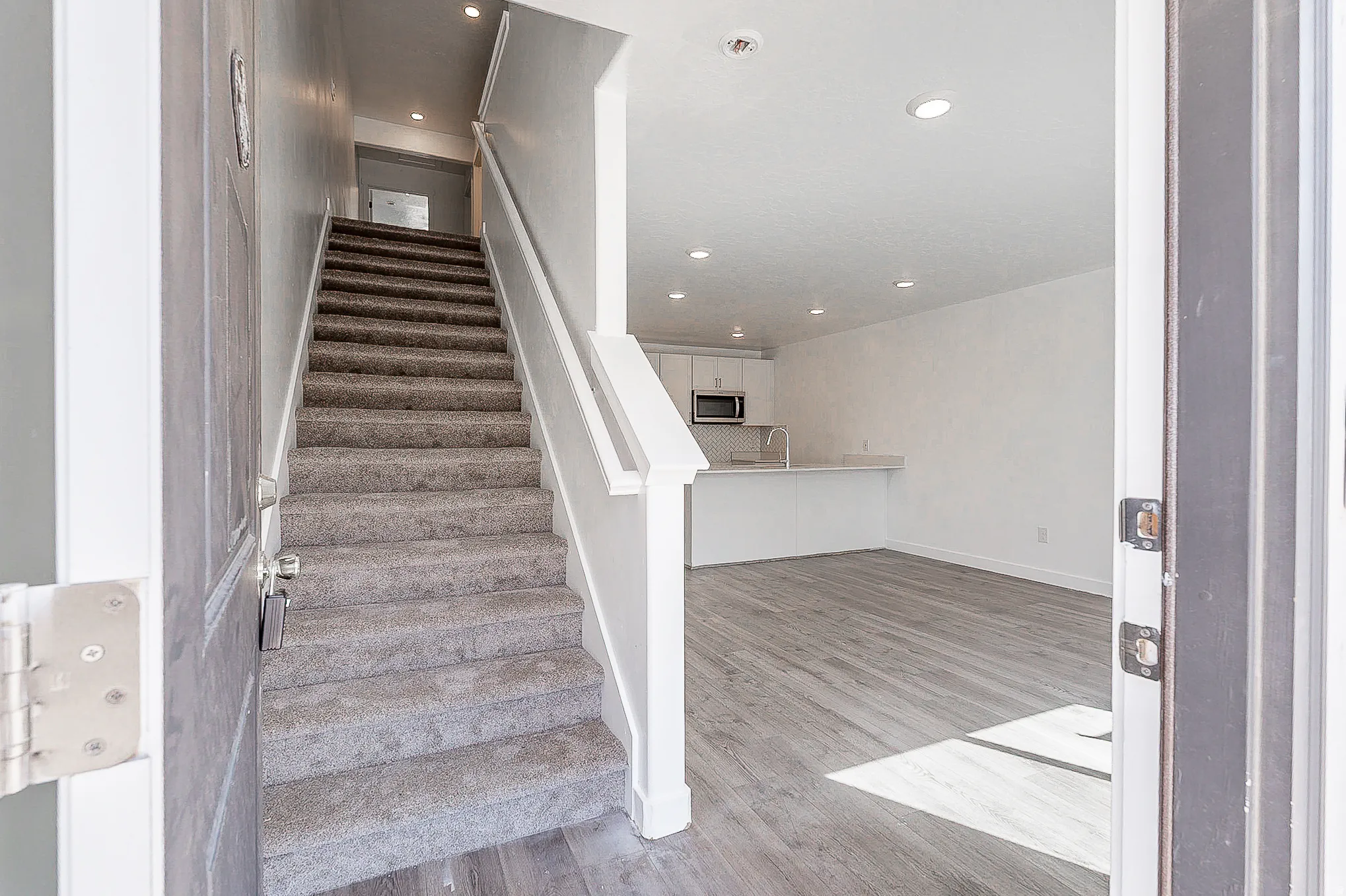 Entryway featuring carpeted stairs with white handrails and wood-finish flooring extending into the living area