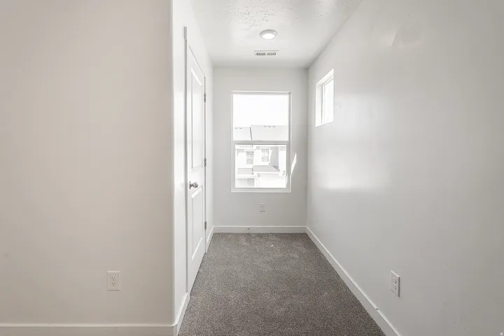 Bright hallway with recessed ceiling lighting, neutral white walls, and gray carpet flooring