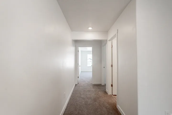Bright hallway with recessed lighting and neutral wall finishes, featuring multiple white six-panel doors and warm wood-finish flooring throughout