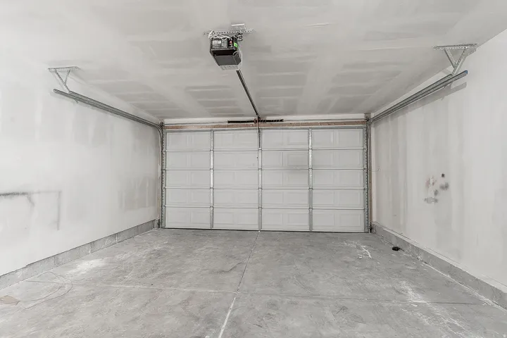 Spacious garage with a sectional overhead door, exposed ceiling joists, concrete flooring, and an automatic garage door opener mechanism