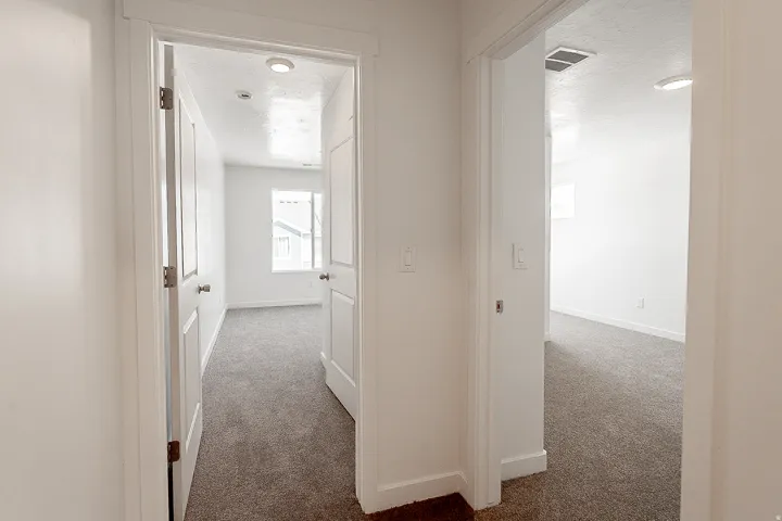 Bright hallway featuring clean white walls, recessed ceiling lighting, and neutral carpet flooring throughout