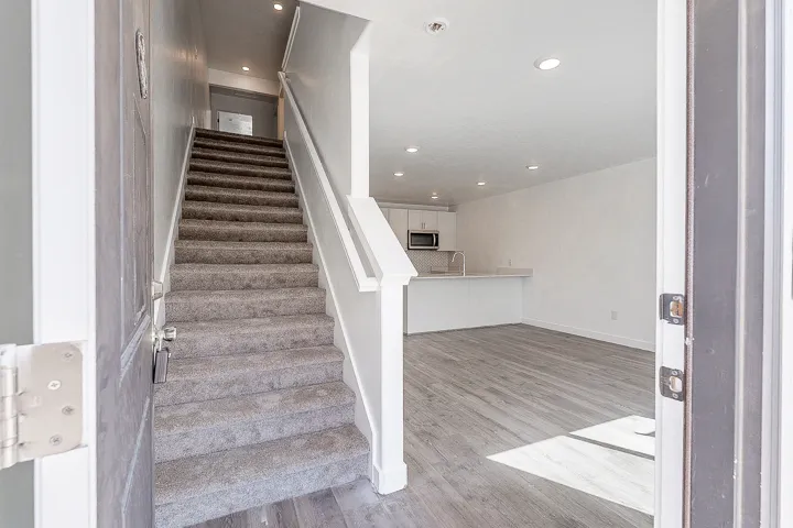 Entryway featuring carpeted stairs with white handrails and wood-finish flooring extending into the living area