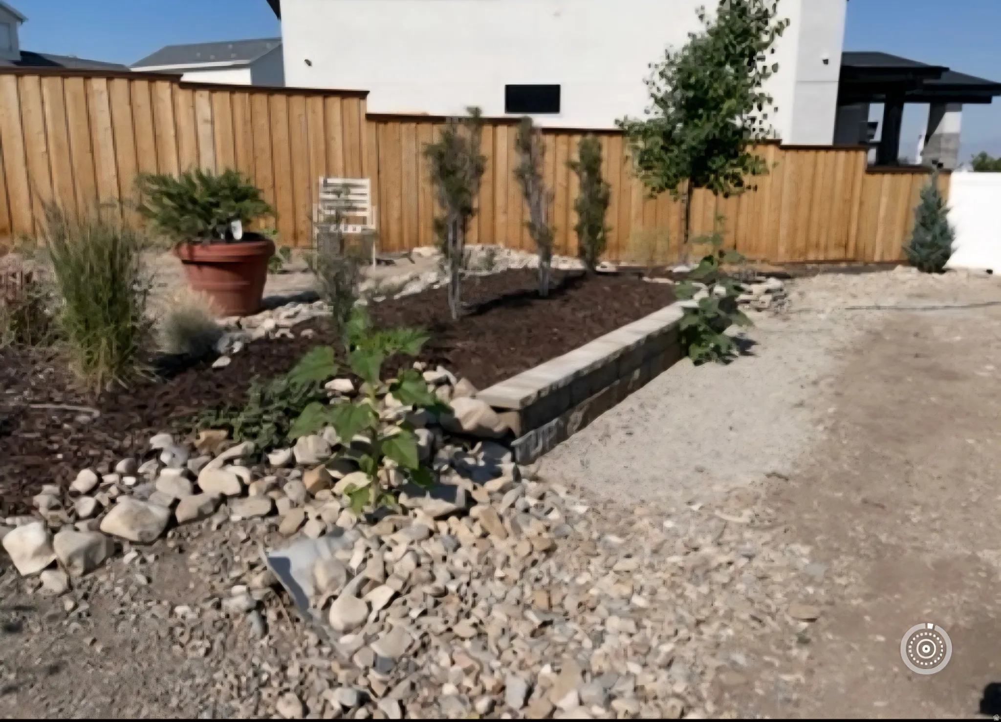Backyard landscape featuring raised planter beds with mature shrubs and ornamental grasses, natural stone hardscaping with river rock accents, wood-finish privacy fencing, and established trees providing structure and definition to the outdoor space