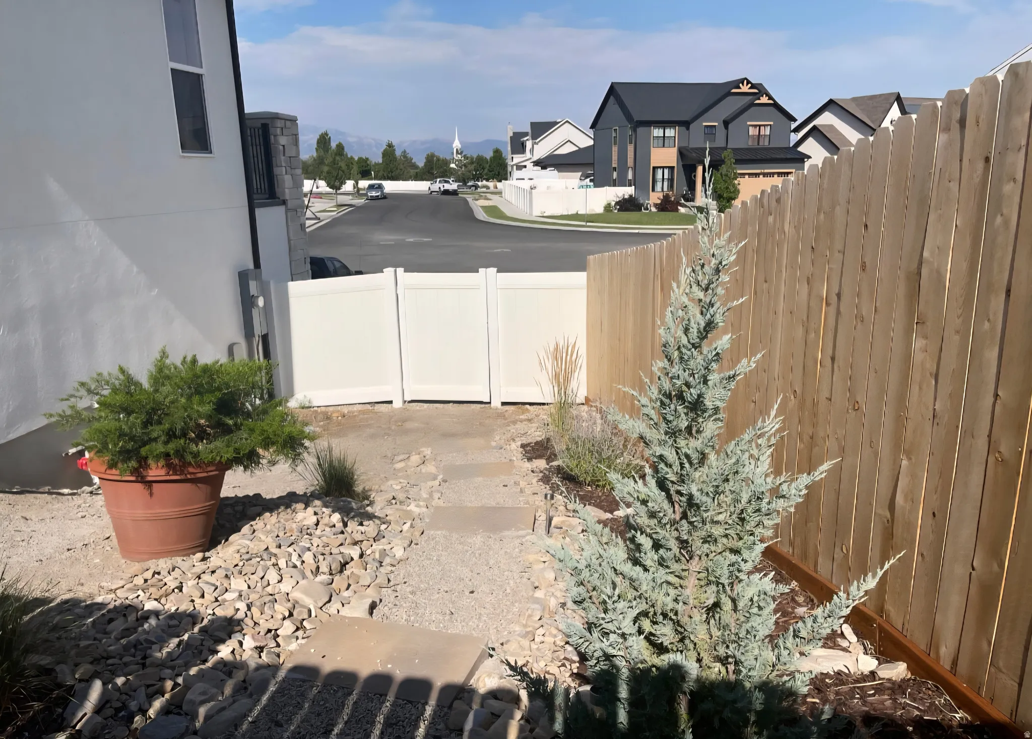 Side yard featuring a gravel and paver pathway, a privacy fence, and planted shrubbery