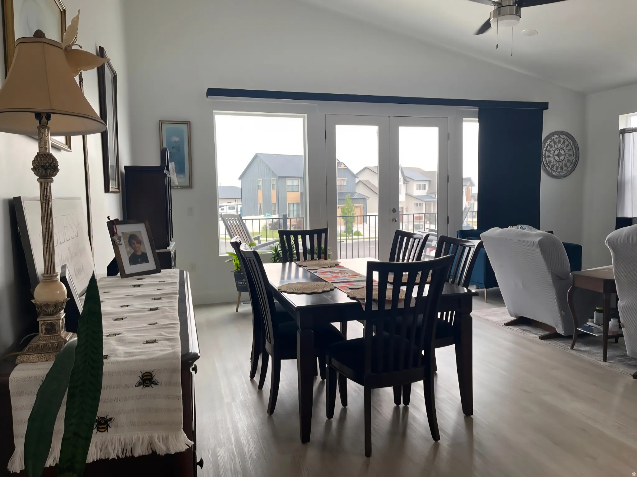 Bright dining area featuring a black wood dining table with seating for six, hardwood flooring throughout, and expansive multi-panel french doors and windows providing natural light and outdoor deck access
