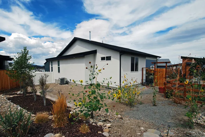 White stucco exterior with black trim, wood fencing, white vinyl fencing, and a gravel pathway