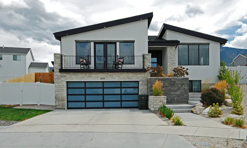Modern façade with a sloped roofline, stucco and stone-finish exterior, full-light garage door, and a second-story balcony