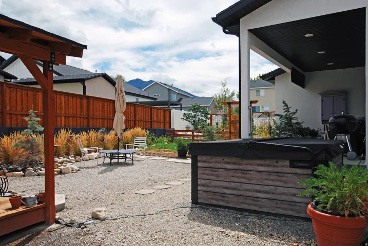 Gravel patio with a built-in spa, wood fence, and mature landscaping