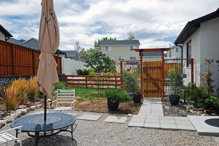 Gravel patio area with paver stone walkway, privacy fencing, and wood gate with overhead arbor