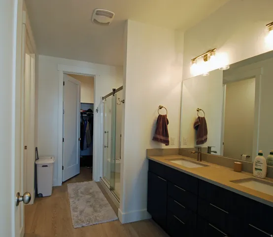 Dual vanity with undermount sinks, wood-finish flooring, and a glass-enclosed shower