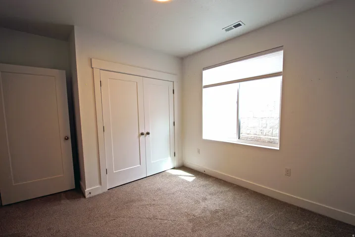 Carpeted room featuring a white paneled door, a bi-fold closet with white paneled doors, and a window with blinds