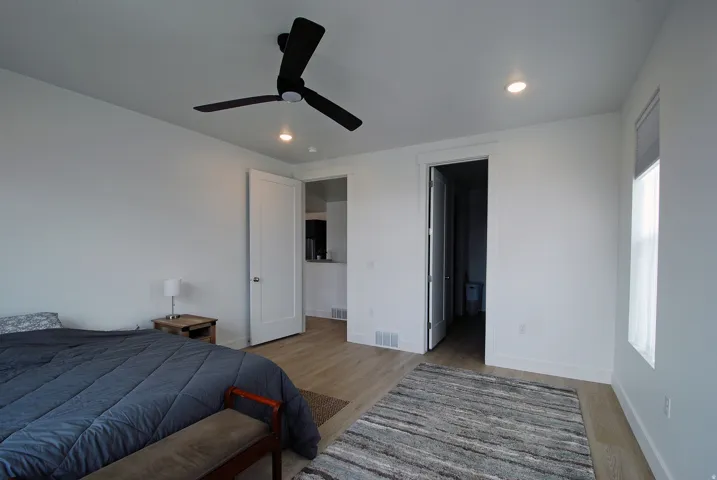 Recessed lighting, black ceiling fan, light wood-finish flooring, white walls, and a window with a roller shade