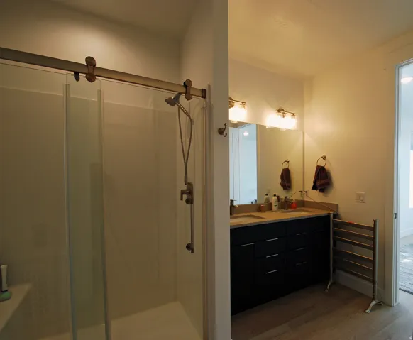 Shower with glass enclosure and sliding barn door hardware, double vanity with dark cabinetry, dual undermount sinks, and light-toned countertop