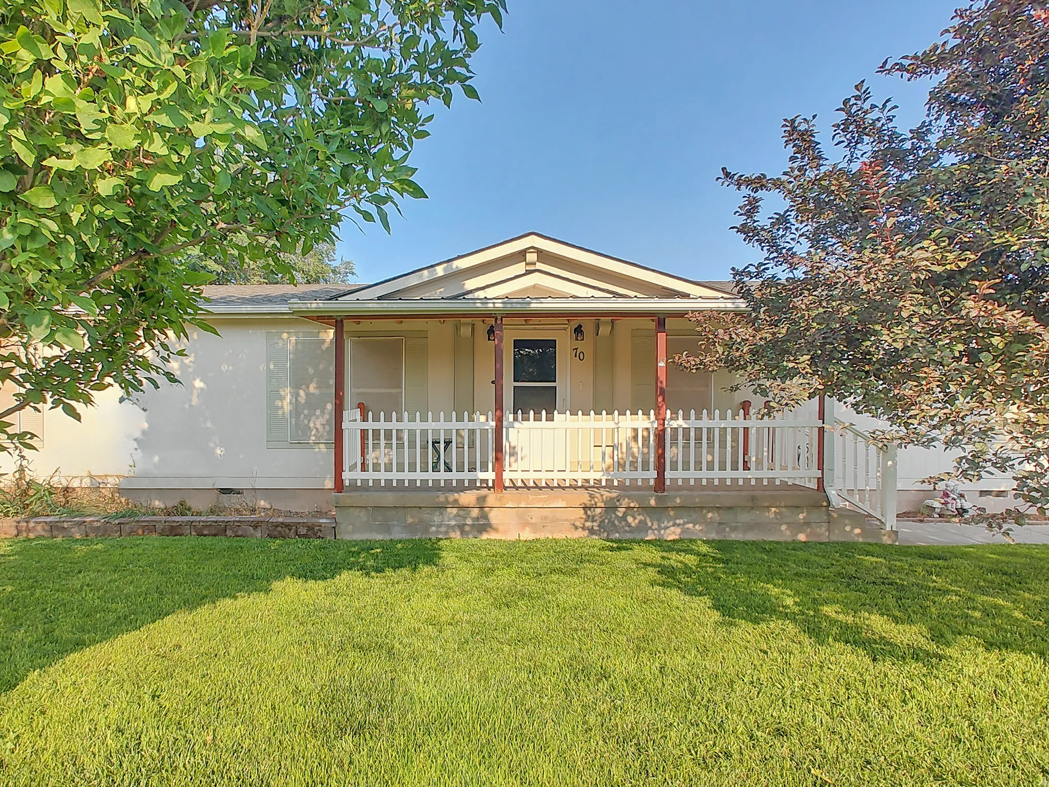 Charming single-story home featuring a welcoming front porch with white railings and columns, gable roofline, and a manicured lawn framed by mature landscaping