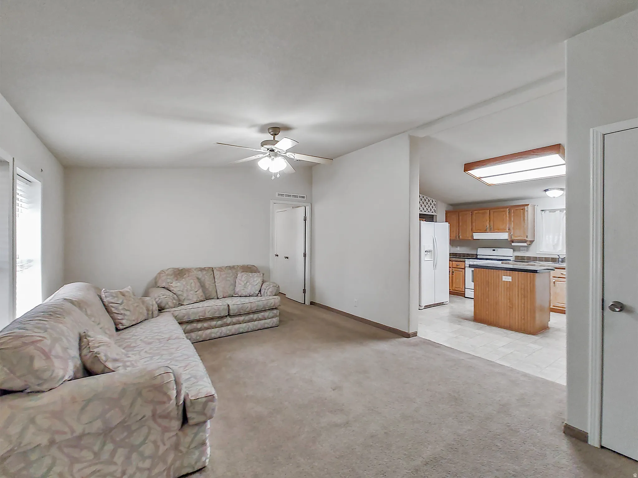 Spacious living area with ceiling fan light fixture and carpet flooring