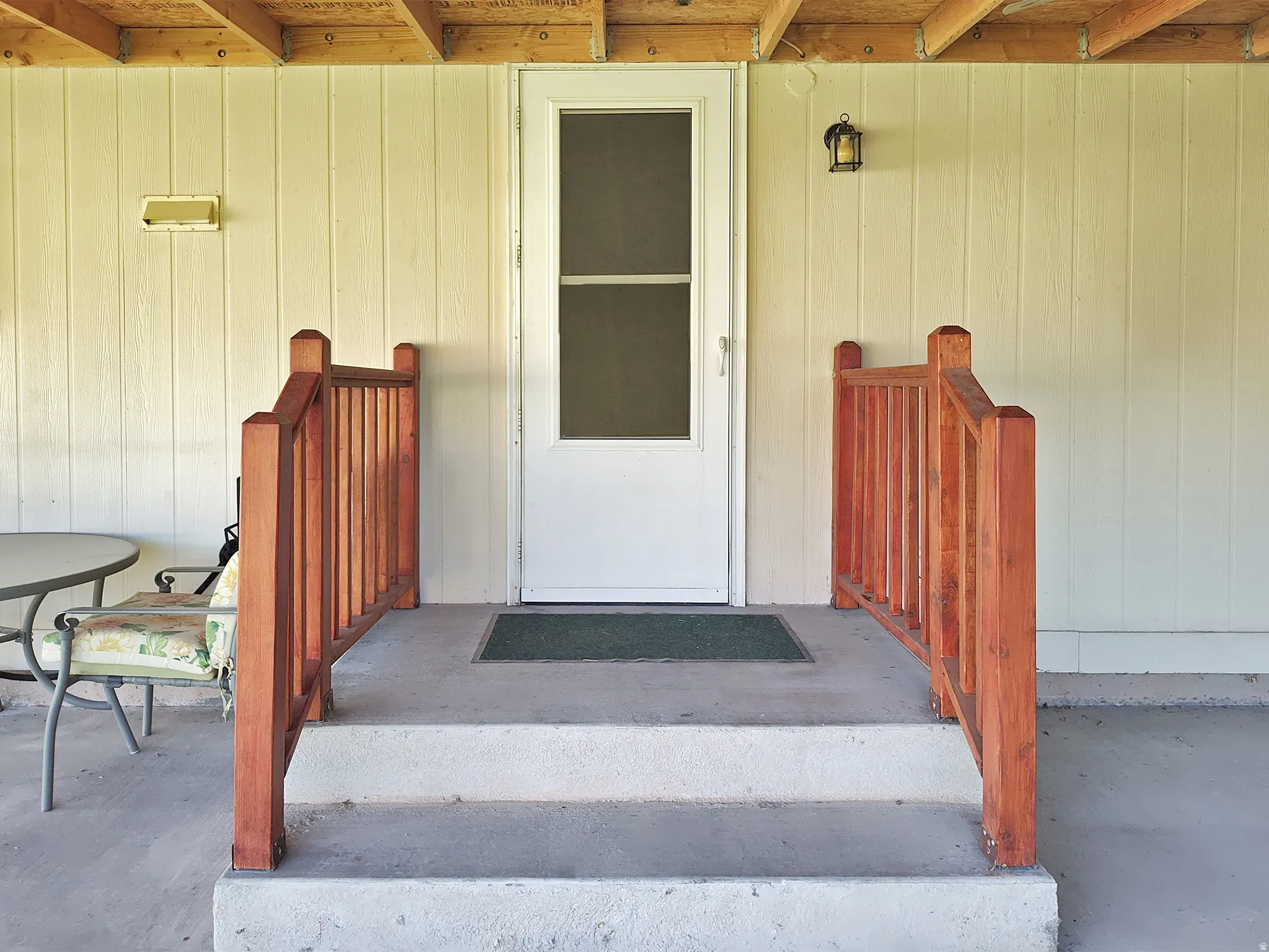 Backyard entryway featuring a white screen door, light-colored vertical siding, and a covered concrete porch
