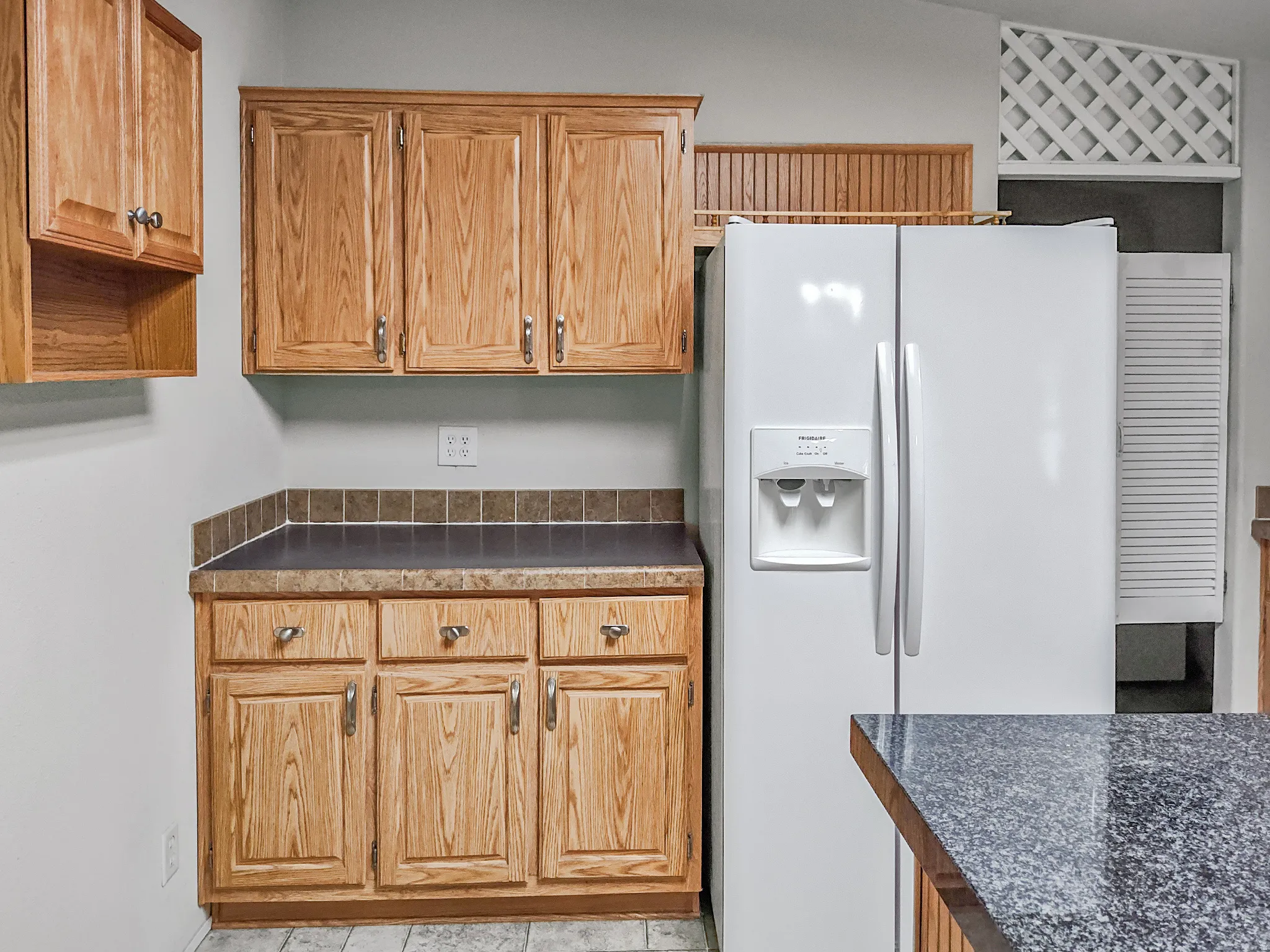 Kitchen featuring wood-finish cabinetry, a white side-by-side refrigerator, dark countertops, and a tiled backsplash