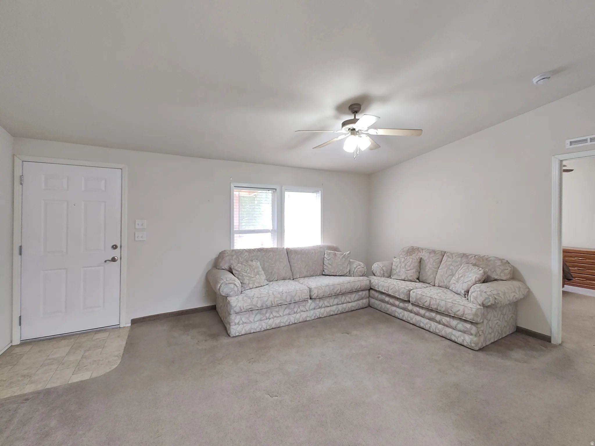 Living area featuring a ceiling fan with light fixture, neutral carpeting, and a white paneled entry door with hardware